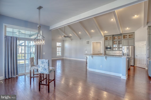 kitchen featuring ceiling fan, decorative light fixtures, beam ceiling, stainless steel appliances, and light stone counters