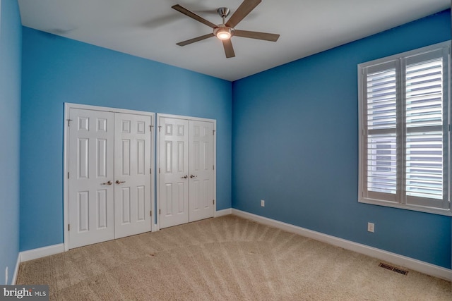 unfurnished bedroom with ceiling fan, light carpet, and two closets