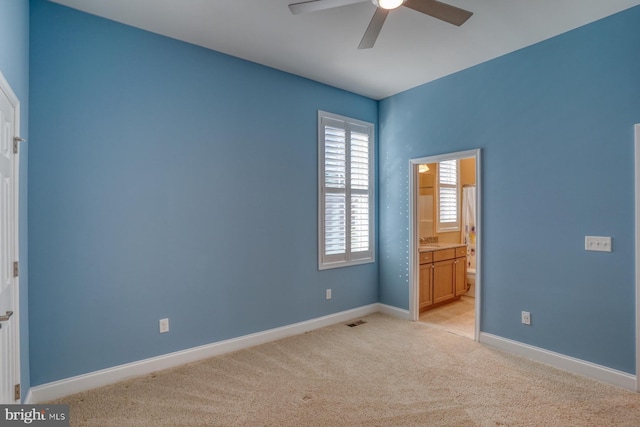 unfurnished bedroom featuring ceiling fan, ensuite bathroom, and light colored carpet