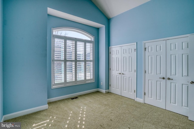 unfurnished bedroom featuring light carpet, multiple closets, and lofted ceiling