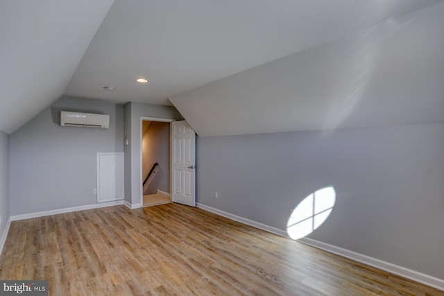 additional living space with light hardwood / wood-style floors, a wall mounted air conditioner, and vaulted ceiling