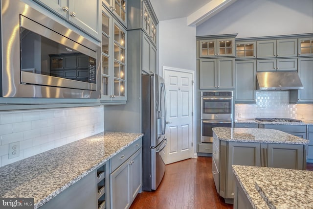 kitchen featuring appliances with stainless steel finishes, backsplash, dark wood-type flooring, light stone counters, and a kitchen island