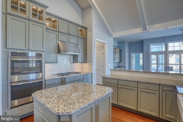 kitchen featuring light stone countertops, appliances with stainless steel finishes, tasteful backsplash, a kitchen island, and dark hardwood / wood-style flooring