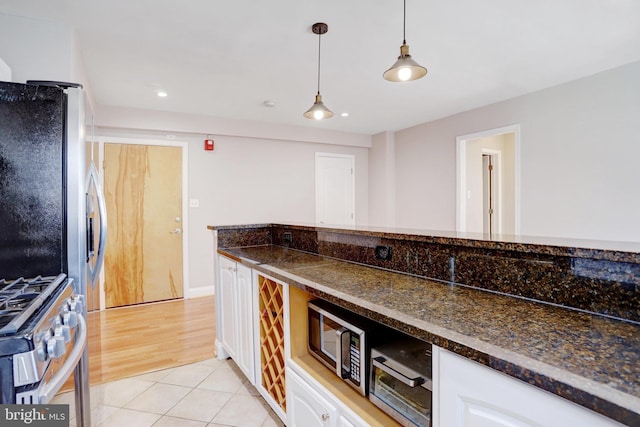 kitchen featuring light tile patterned floors, white cabinetry, dark stone countertops, stainless steel appliances, and decorative light fixtures