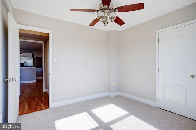 unfurnished bedroom with ceiling fan, stainless steel fridge with ice dispenser, and light carpet