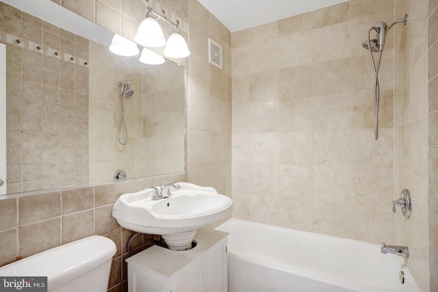 full bathroom with tile walls, sink, tiled shower / bath combo, and toilet