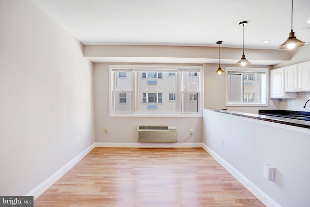 kitchen with light wood-type flooring, pendant lighting, white cabinets, and a wall unit AC