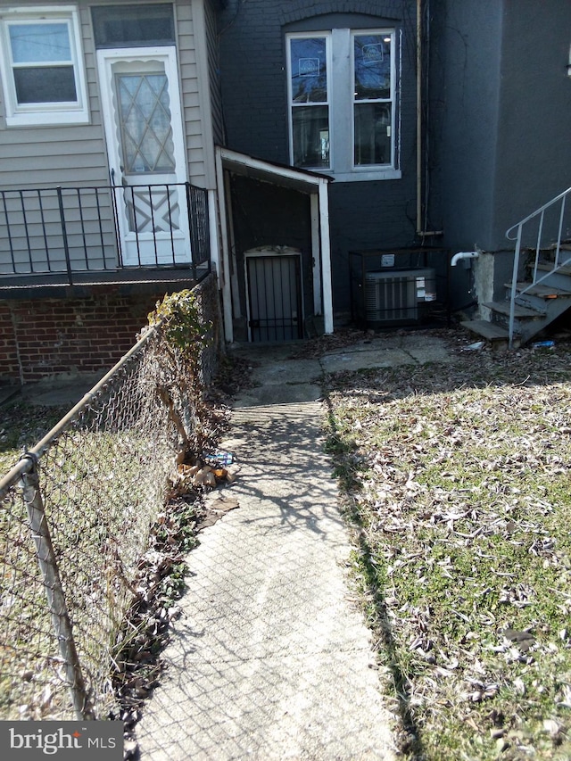 property entrance with brick siding, central AC unit, and fence