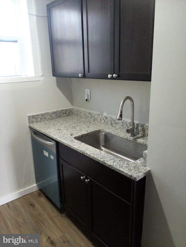 kitchen with dark wood-style flooring, a sink, light stone countertops, dishwasher, and baseboards