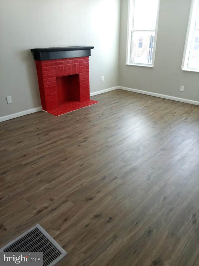 unfurnished living room with dark wood-type flooring, visible vents, plenty of natural light, and a fireplace