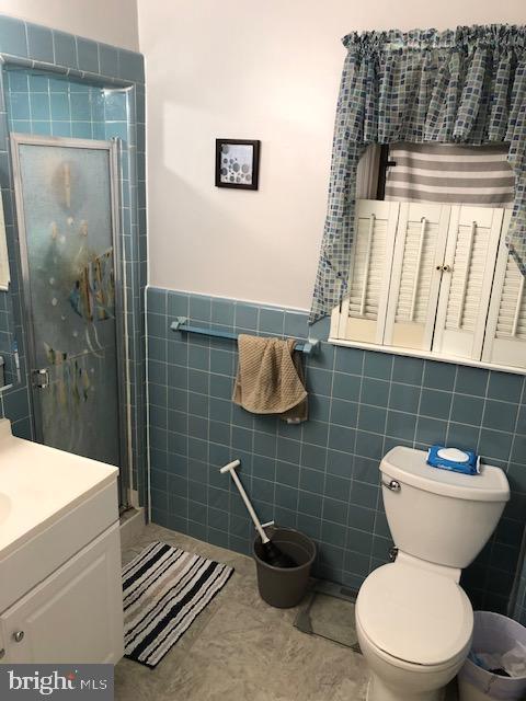 bathroom with vanity, toilet, a shower with door, and tile walls