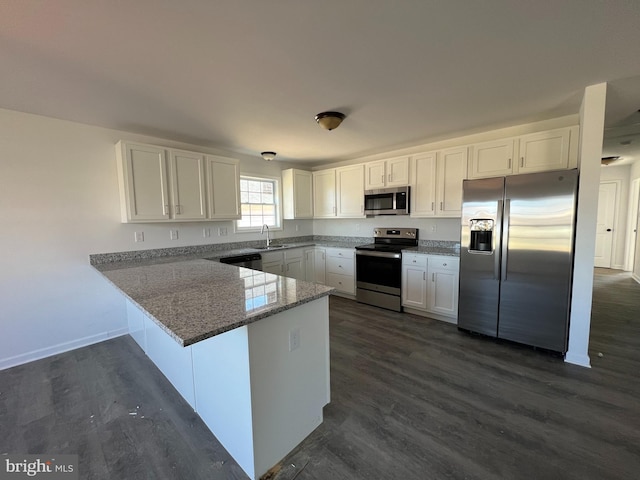 kitchen featuring stainless steel appliances, a peninsula, white cabinetry, and light stone countertops