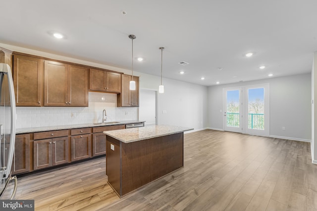 kitchen with light stone countertops, a center island, sink, light hardwood / wood-style flooring, and decorative light fixtures