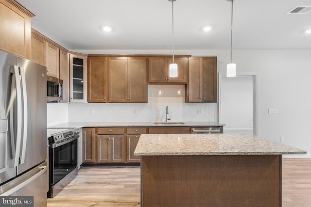 kitchen with light wood-type flooring, light stone counters, stainless steel appliances, sink, and decorative light fixtures