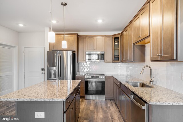 kitchen with dark wood-type flooring, hanging light fixtures, sink, appliances with stainless steel finishes, and a kitchen island