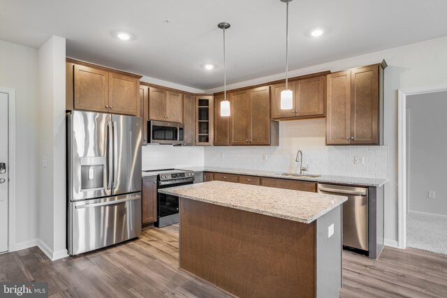 kitchen with decorative light fixtures, stainless steel appliances, light hardwood / wood-style flooring, and sink