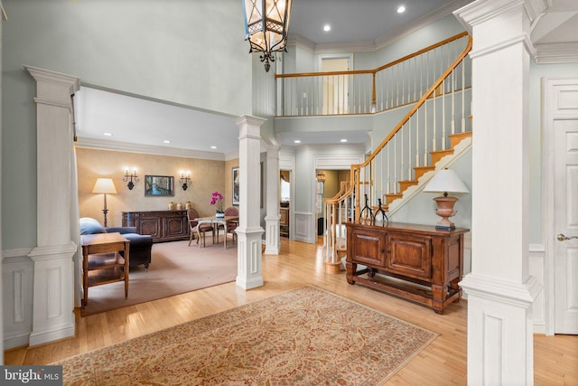 entryway featuring stairs, ornamental molding, decorative columns, wood finished floors, and a decorative wall