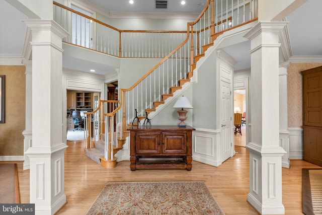 stairs with wood finished floors, visible vents, ornate columns, wainscoting, and crown molding