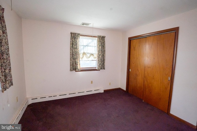 unfurnished bedroom featuring dark carpet, baseboard heating, and a closet