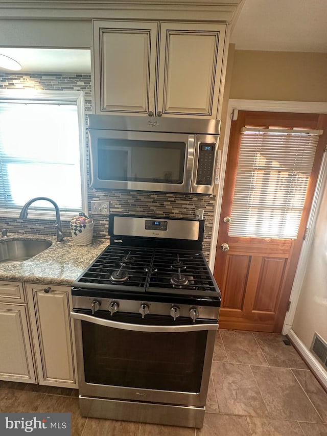 kitchen featuring sink, cream cabinets, light stone counters, decorative backsplash, and appliances with stainless steel finishes