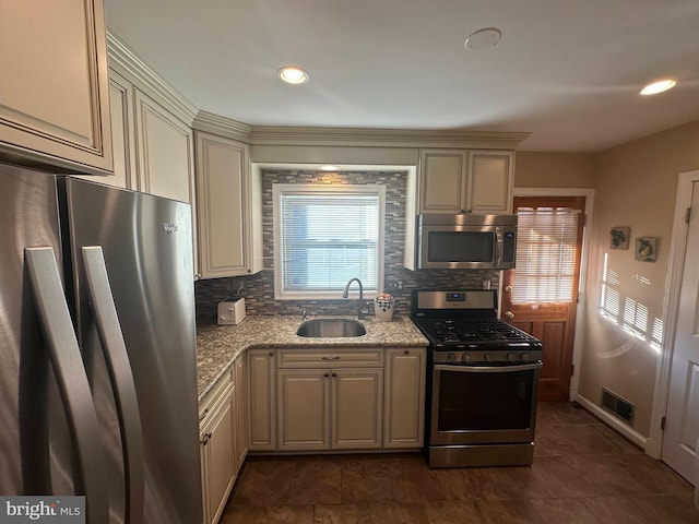 kitchen with appliances with stainless steel finishes, light stone countertops, sink, cream cabinets, and tasteful backsplash