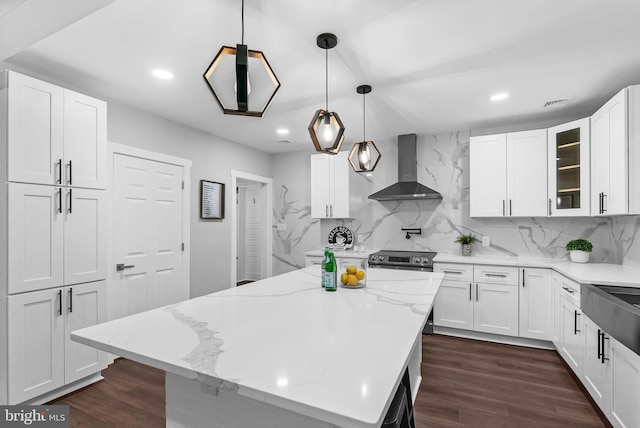 kitchen featuring white cabinetry, a center island, wall chimney exhaust hood, hanging light fixtures, and light stone counters