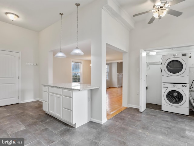 kitchen with light stone countertops, white cabinetry, ceiling fan, pendant lighting, and stacked washer and clothes dryer