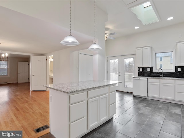 kitchen featuring white dishwasher, white cabinets, hanging light fixtures, a kitchen island, and light stone counters