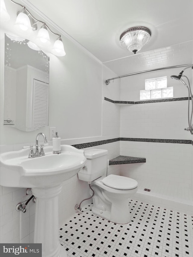 bathroom with tile patterned flooring, a tile shower, toilet, and tile walls