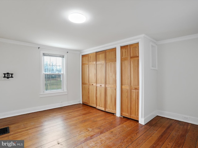 unfurnished bedroom with hardwood / wood-style floors, ornamental molding, and two closets