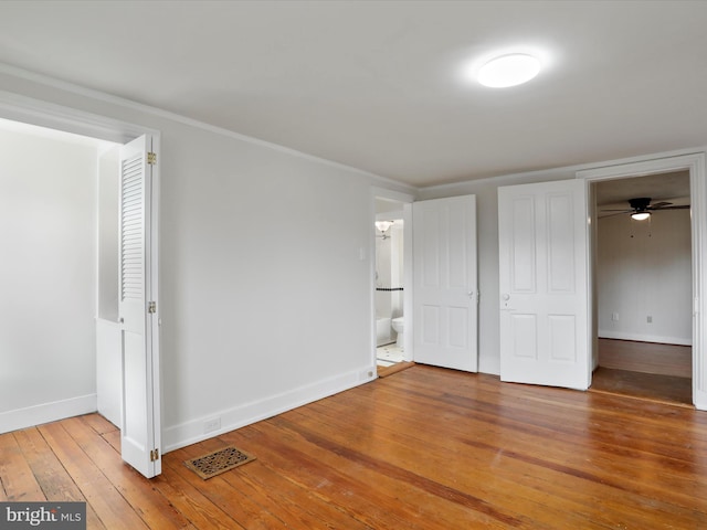 unfurnished bedroom featuring hardwood / wood-style flooring, ensuite bath, and crown molding