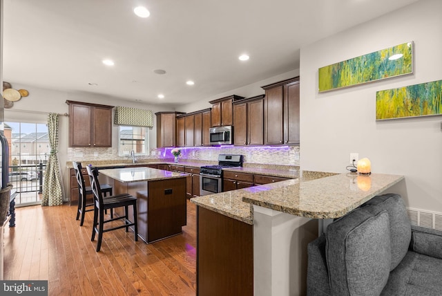 kitchen with light stone countertops, a center island, stainless steel appliances, kitchen peninsula, and a breakfast bar