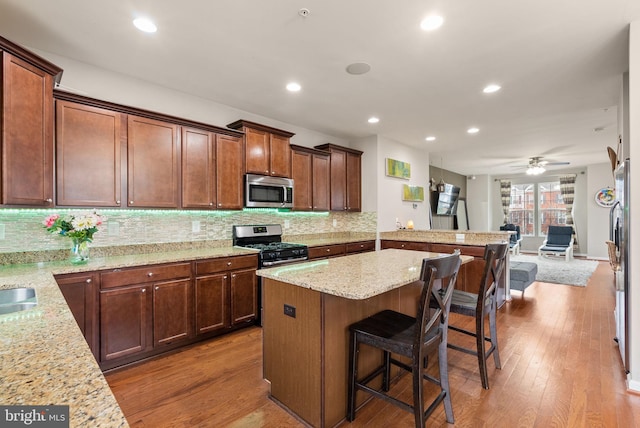 kitchen featuring kitchen peninsula, light stone counters, stainless steel appliances, ceiling fan, and a breakfast bar area