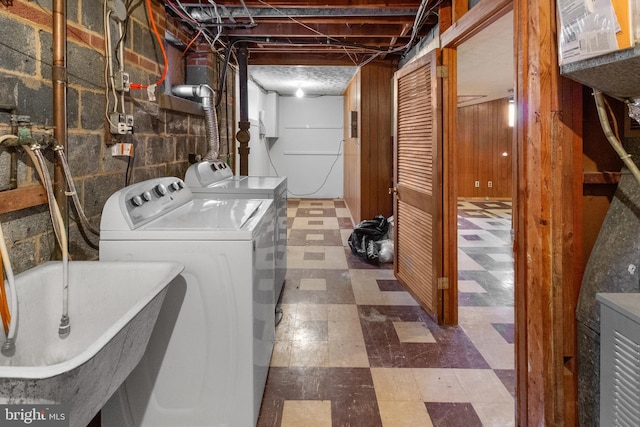 clothes washing area with wood walls, washing machine and dryer, and sink