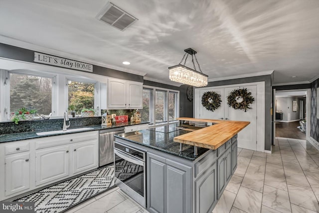 kitchen with pendant lighting, white cabinets, sink, butcher block countertops, and a kitchen island