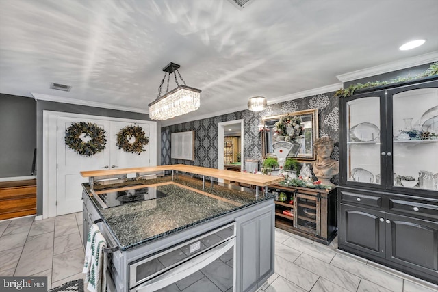 kitchen with black electric stovetop, dark stone counters, ornamental molding, decorative light fixtures, and a kitchen island