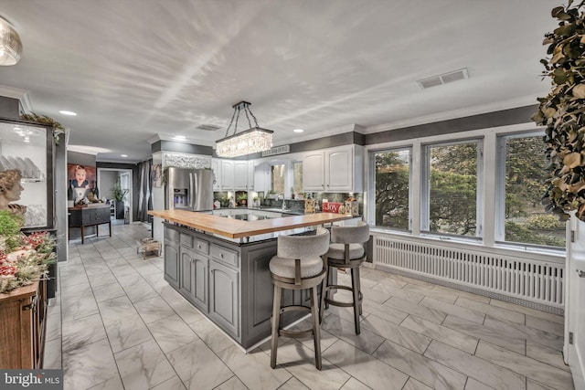 kitchen with butcher block counters, hanging light fixtures, a kitchen breakfast bar, stainless steel fridge with ice dispenser, and white cabinets