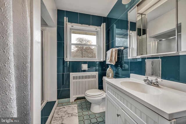 bathroom with radiator, vanity, a shower with shower door, and toilet