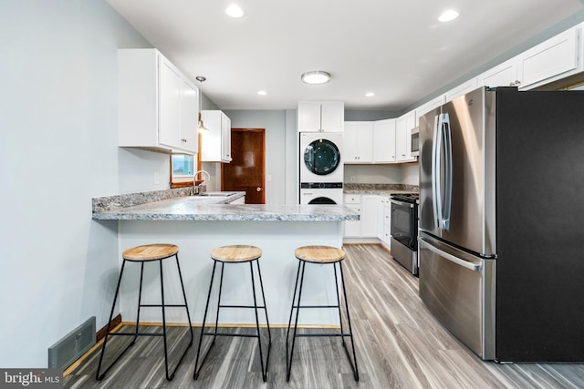 kitchen with white cabinets, kitchen peninsula, stainless steel appliances, and stacked washer and clothes dryer