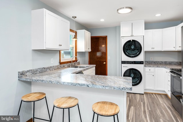 kitchen featuring white cabinetry, sink, kitchen peninsula, stacked washer / drying machine, and a breakfast bar