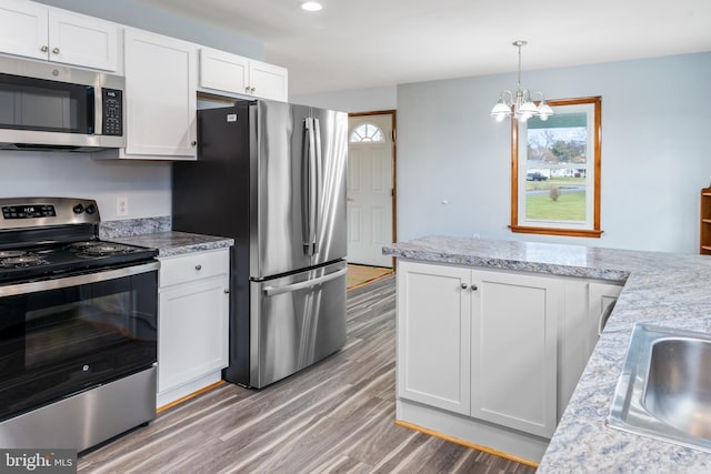 kitchen with an inviting chandelier, white cabinets, sink, light hardwood / wood-style flooring, and appliances with stainless steel finishes