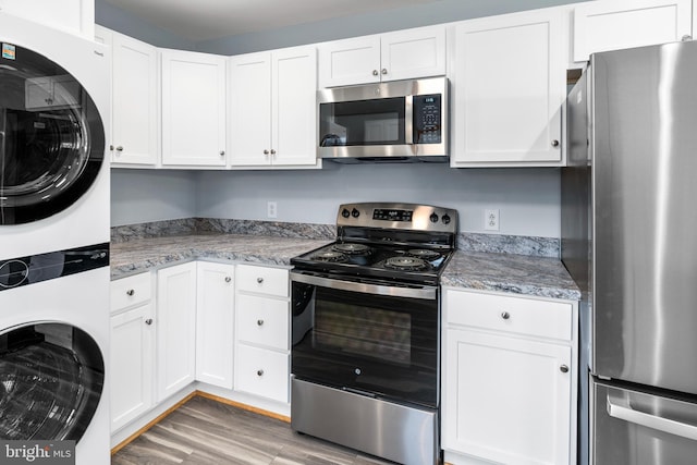 kitchen featuring white cabinetry, light stone countertops, hardwood / wood-style floors, stacked washer / drying machine, and appliances with stainless steel finishes