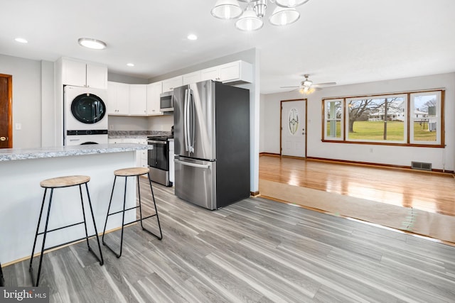 kitchen with appliances with stainless steel finishes, stacked washer / drying machine, a kitchen bar, white cabinets, and light wood-type flooring