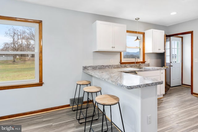 kitchen featuring white cabinetry, sink, pendant lighting, light hardwood / wood-style floors, and a kitchen bar