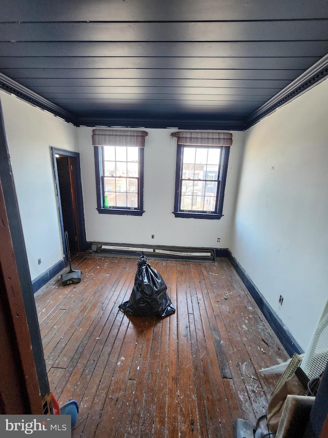 empty room featuring baseboard heating, dark wood-type flooring, a wealth of natural light, and ornamental molding