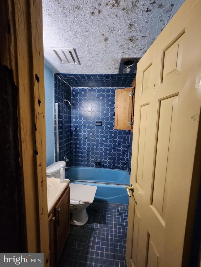 full bathroom with vanity, toilet, a textured ceiling, and tiled shower / bath combo