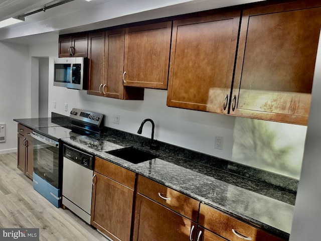 kitchen featuring sink, light wood-type flooring, stainless steel appliances, and dark stone counters