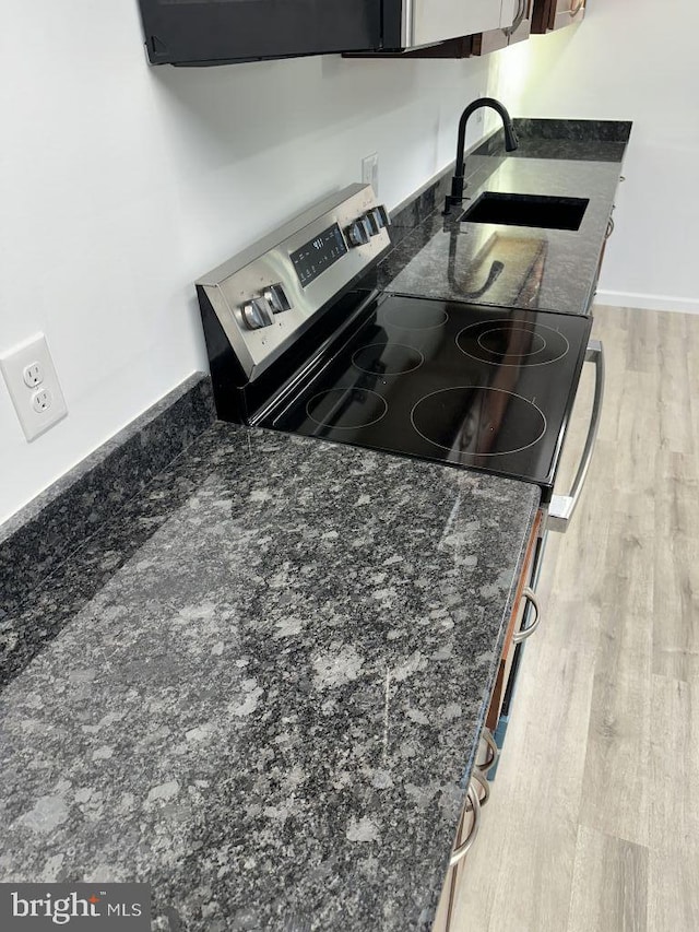 kitchen with stainless steel electric stove, light wood-type flooring, sink, and dark stone counters