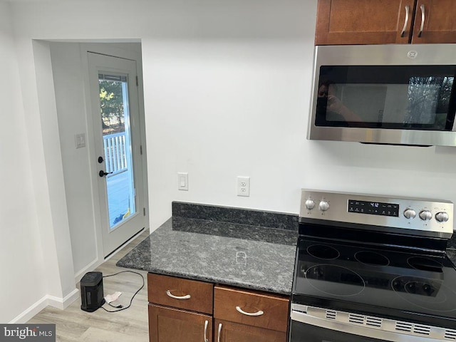 kitchen featuring stainless steel appliances, light hardwood / wood-style flooring, and dark stone counters