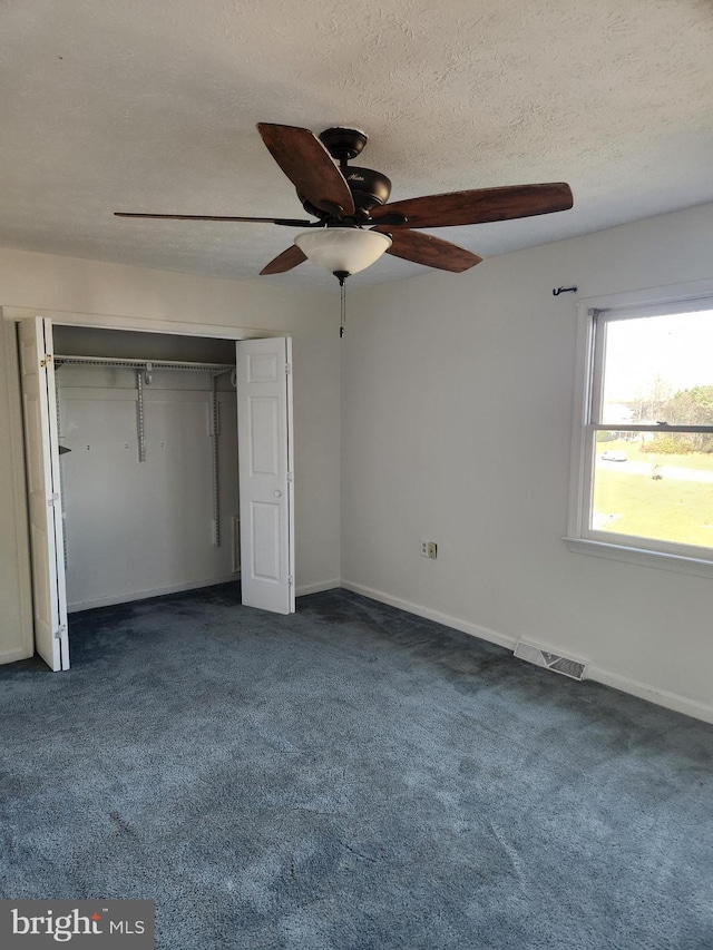 unfurnished bedroom with a textured ceiling, a closet, dark carpet, and ceiling fan